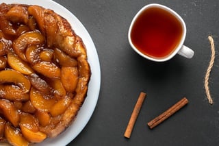 tarte tatin with peaches and caramel on white plate on dark background next to the white cup
